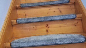 Eine Holztreppe mit blauen Teppichläufern, die zu einer Zwischenebene führen.