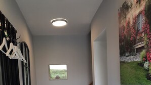 Ein Flur mit gefliestem Boden, einem Kleiderständer, einem kleinen Tisch mit Stuhl, einem Heizkörper und einem Bild von einem Garten.