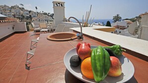A rooftop terrace with a plate of fruit, a sink, and a view of a coastal town. - Pinomar 1A (Nerja)