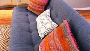 A grey sofa with three colorful knitted throw pillows and a patterned cushion.