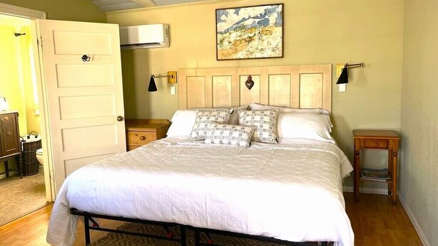 A bedroom with a bed, bedside tables, a nightstand, a door, and an air conditioning unit.