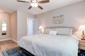 A bedroom with a large bed, a ceiling fan, a wall-mounted macrame decoration, and a bedside lamp.