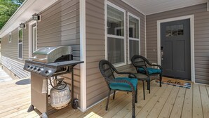 En inglasad veranda med en grill, två flätade fåtöljer och en dörr med en välkomstmatta där det står ”hej”.