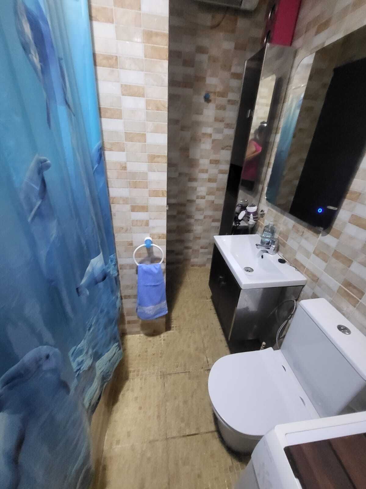 A small bathroom with a tiled wall, a sink, a toilet, and a mirror.