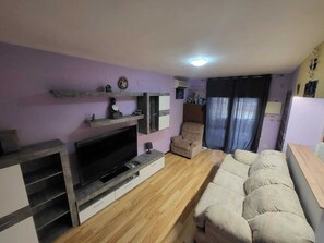 A living room with a TV, sofa, and wooden flooring.
