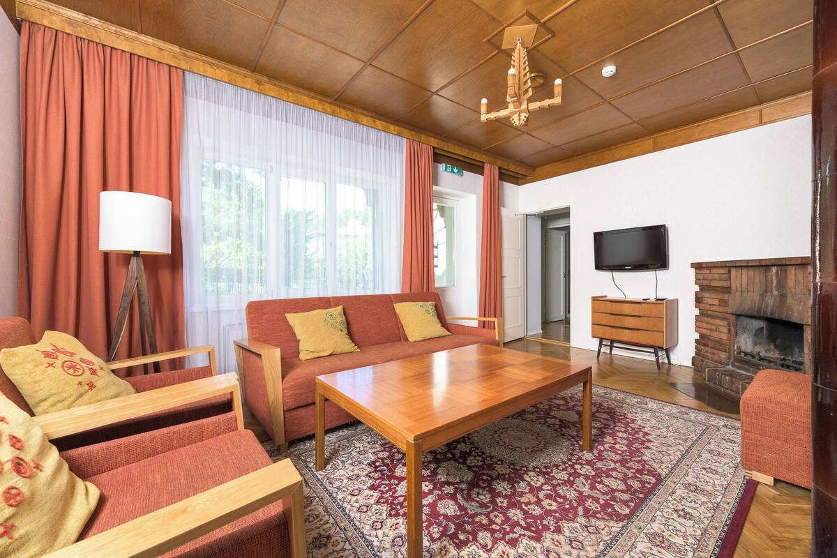 A cozy living room with a wooden coffee table, red sofas, a patterned rug, a fireplace, and a television.