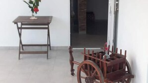 Une pièce comprenant un chariot en bois, une table ornée d’un vase de fleurs et une porte donnant sur une autre pièce.