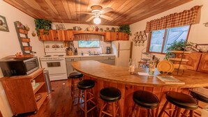 Une cuisine avec des meubles en bois, un îlot central doté de tabourets, un four à micro-ondes, une cuisinière, un réfrigérateur et divers ustensiles de cuisine.