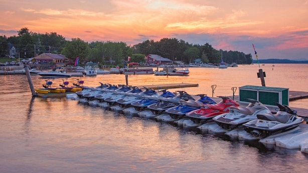 Un port de plaisance avec des bateaux amarrés à des quais en bois, un petit bâtiment et un coucher de soleil sur l’eau.