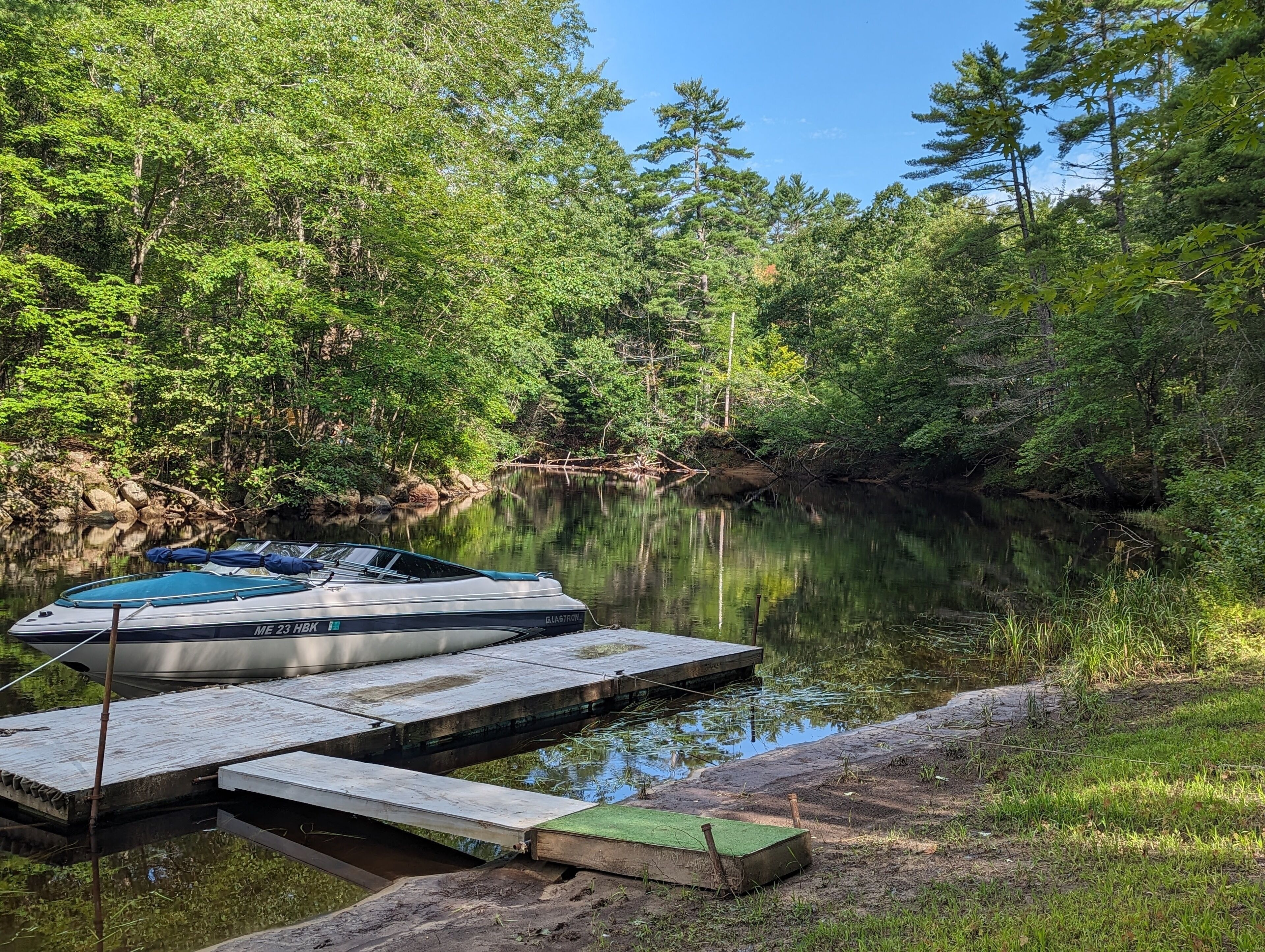 Un bateau était amarré à une jetée en bois qui s’étendait dans une rivière paisible, bordée d’une forêt dense.