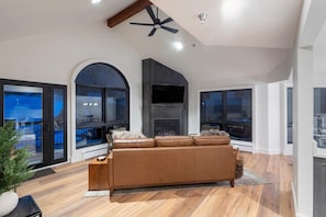 A modern living room with a large sofa, a fireplace, and a ceiling fan. - Le Chamonix A 2 Bedroom Condo (Mountain Village)