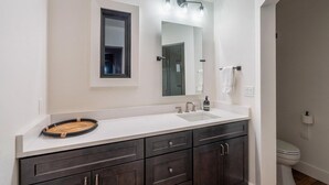 Un baño moderno con tocador blanco, muebles oscuros, un espejo grande y un inodoro.