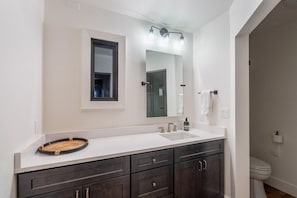 Un baño moderno con tocador blanco, muebles oscuros, un espejo grande y un inodoro.