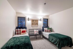 Habitación con dos camas, cada una con una colcha verde y varias almohadas, una mesita y un letrero en la pared.