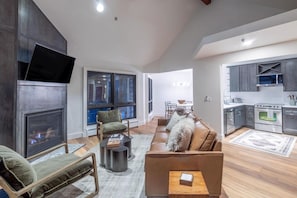 Una sala de estar moderna con chimenea, un sofá, un televisor y una zona de cocina con microondas y horno.