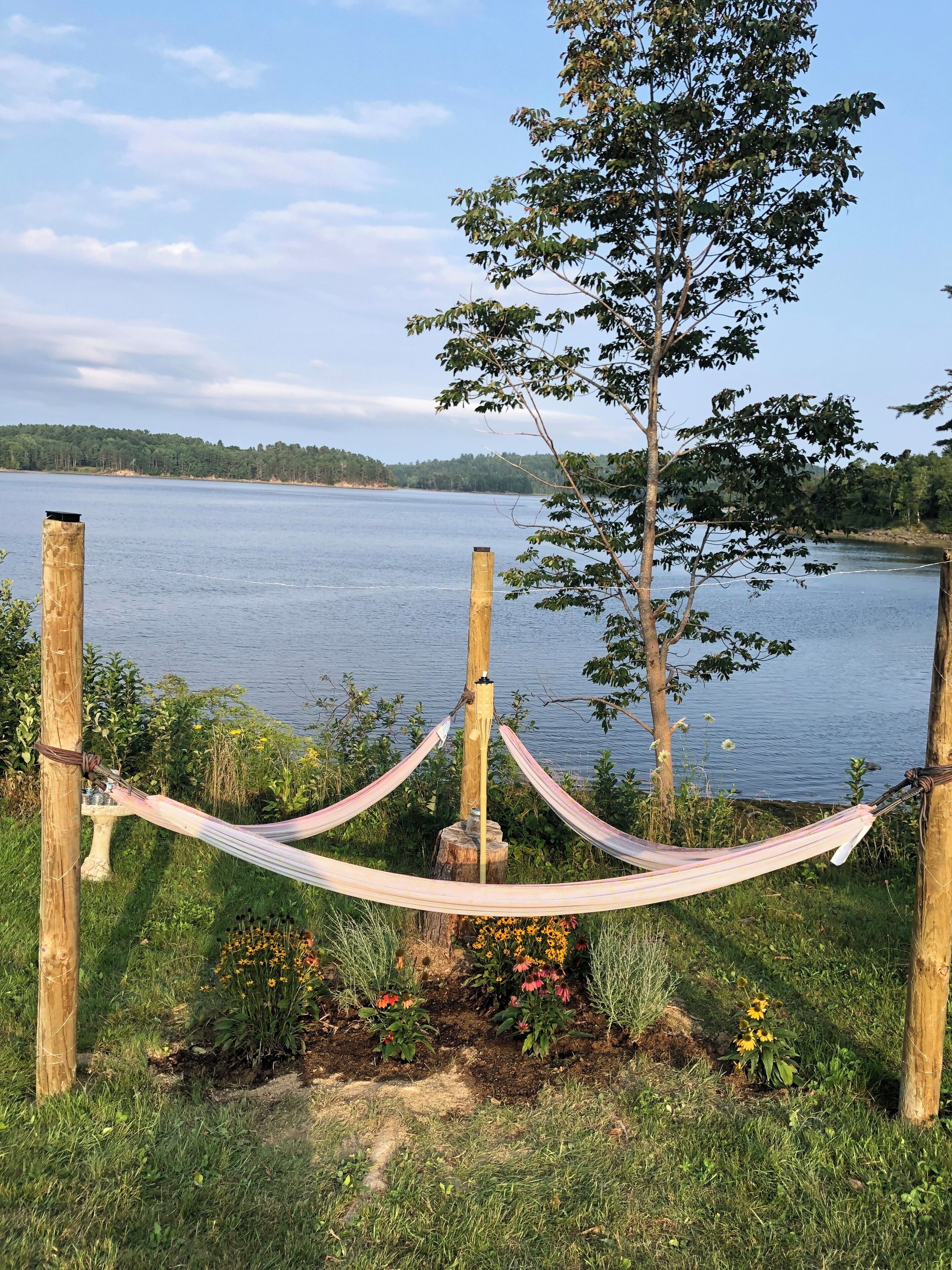 Eine Hängematze, die zwischen Holzbalken gespannt ist, mit einem See und Bäumen im Hintergrund.