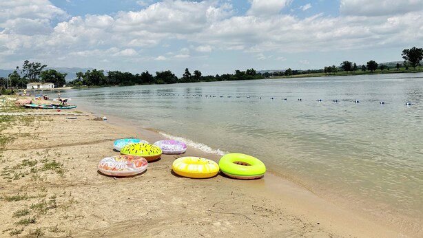 Une plage avec plusieurs bouées gonflables aux couleurs vives et, en arrière-plan, un lac paisible.