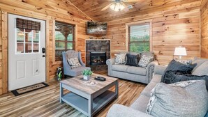 A cozy log cabin interior with a fireplace, a ceiling fan, and a television mounted above it. - Free Dollywood Tix/Pool/5Min2Dollywood/Pool Table (PIgeon Forge)