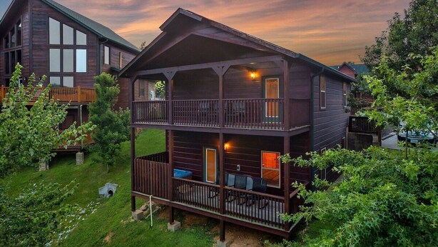 A two-story wooden cabin with a balcony, surrounded by greenery. - Free Dollywood Tix/Pool/5Min2Dollywood/Pool Table (PIgeon Forge)