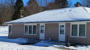 A single-story building with a snow-covered roof and a small porch area. - Northwoods Lodge Hotel Room 1 (Long Lake)