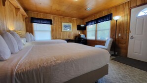 A room with two beds, wooden walls, a desk with a chair, a TV, and a door. - Northwoods Lodge Hotel Room 1 (Long Lake)