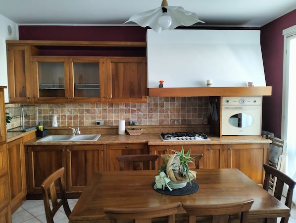 Una cocina con armarios de madera, una estufa a gas, un lavabo y una mesa de comedor con sillas.