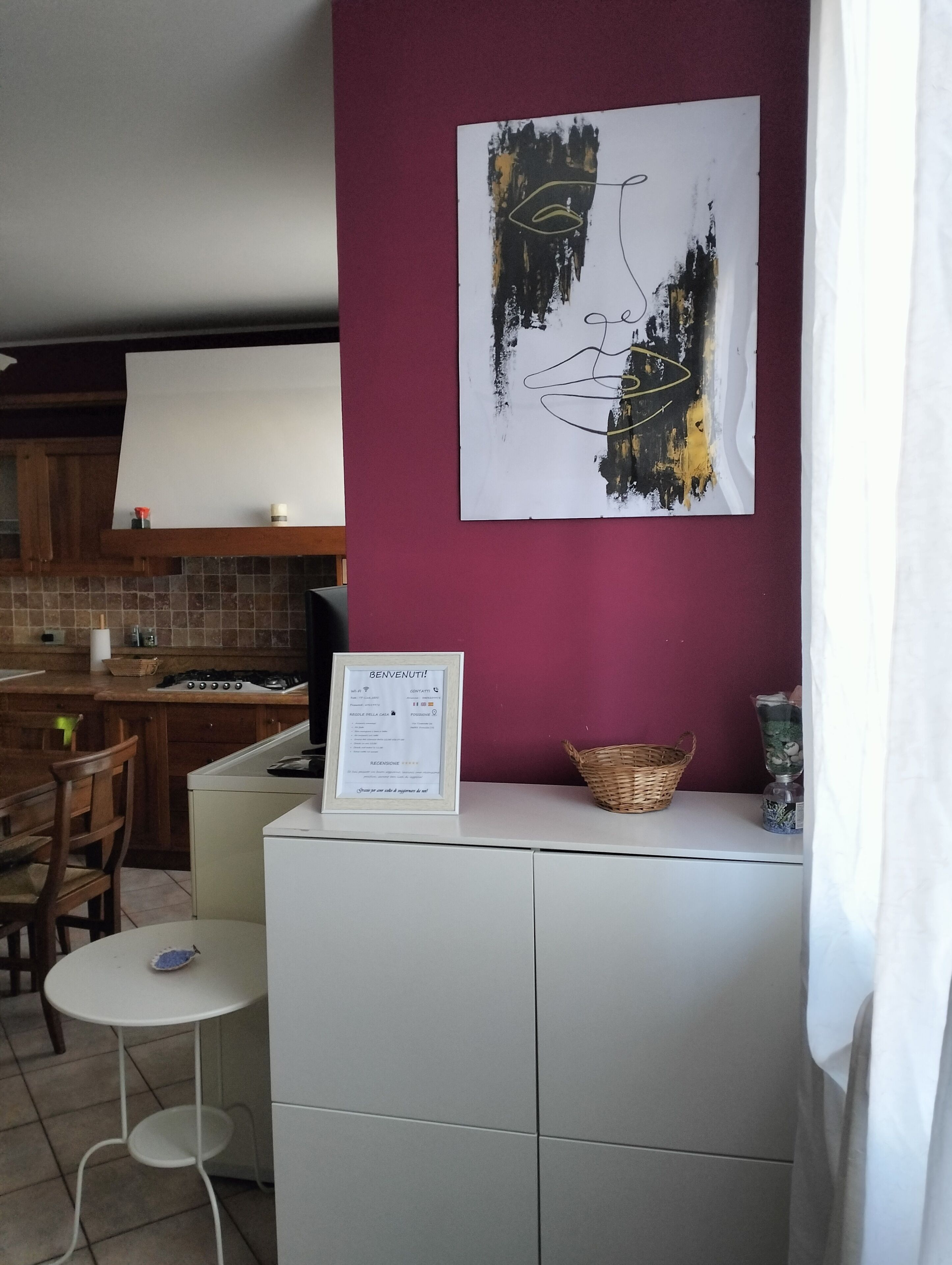 Una cocina con un armario blanco, un cartel de bienvenida enmarcado, una obra de arte en la pared y una cesta de mimbre.