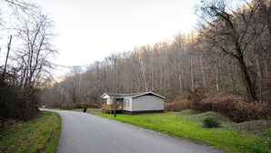 Une maison mobile de plain-pied, dotée d’un porche à l’avant et entourée d’une zone boisée.