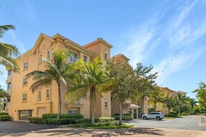 Un hotel de varios pisos con fachada color beige, palmeras y un cielo azul despejado.