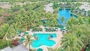 Un resort con piscina central rodeada de palmeras y zonas de descanso.