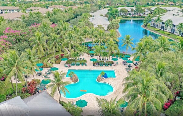 A resort with a central swimming pool surrounded by palm trees and lounge areas.
