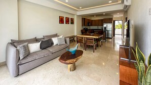 Una sala moderna con un sofá gris, una mesa de centro de madera y una cocina al fondo.