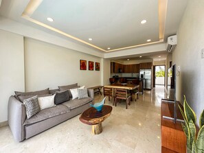 A modern living room with a grey sofa, wooden coffee table, and a kitchen in the background.