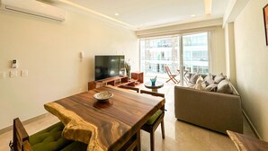 Una sala de estar moderna con una mesa de comedor de madera, sillas verdes, un sofá y una televisión.