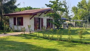 Une petite maison avec un toit rouge et des murs blancs, entourée d’une pelouse bien entretenue et d’arbres.