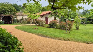 Un chemin de gravier mène à un bâtiment doté d’un toit rouge, entouré de verdure et d’arbres.