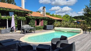 Une piscine avec des chaises longues, une table couverte et un espace barbecue abrité.