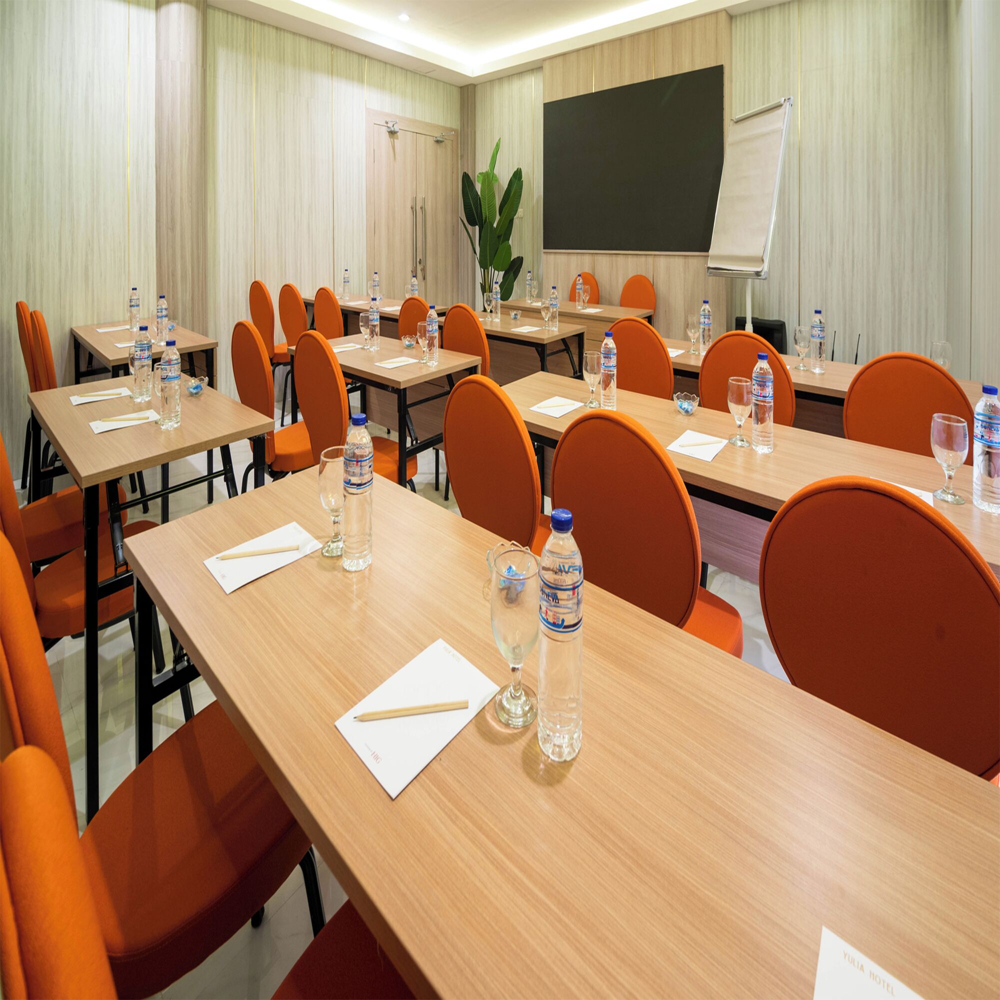 Ein Konferenzraum mit mehreren Tischen und orangefarbenen Stühlen, ausgestattet mit Wasserflaschen und Gläsern.