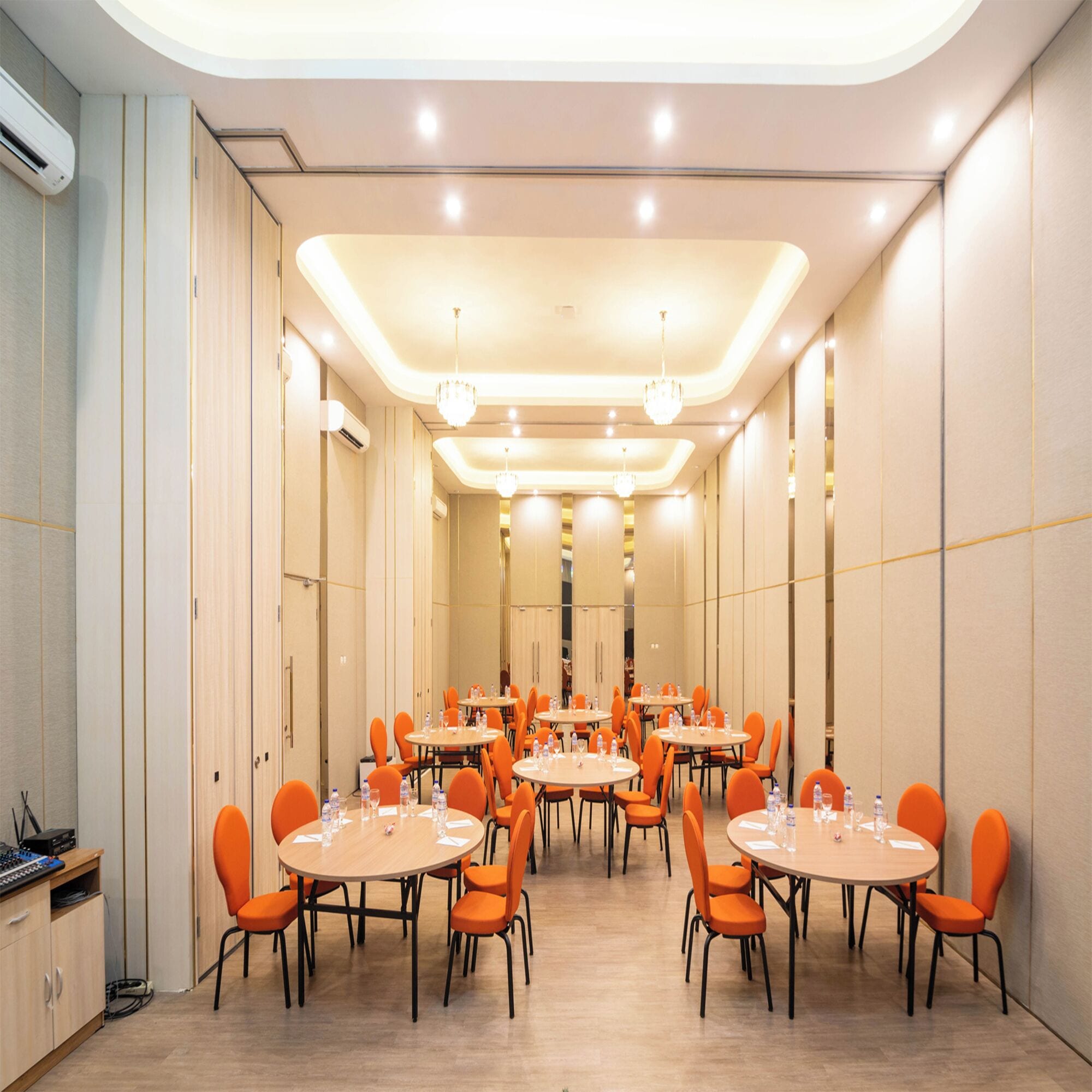 A conference room with multiple tables and orange chairs, equipped with water bottles and glasses.