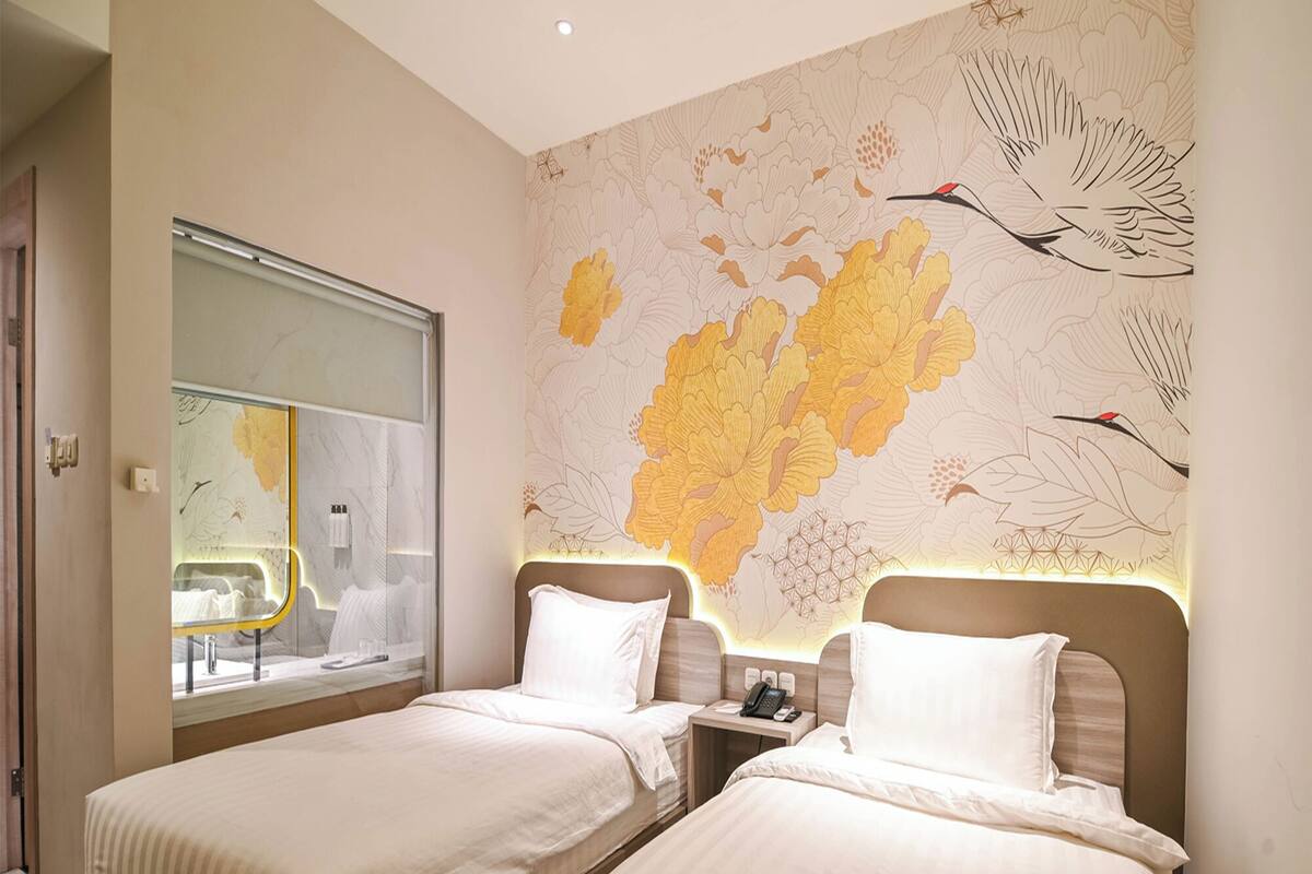 Een hotelkamer met twee bedden, een groot raam en een muur met een bloemen- en vogelmuurdecoratie.