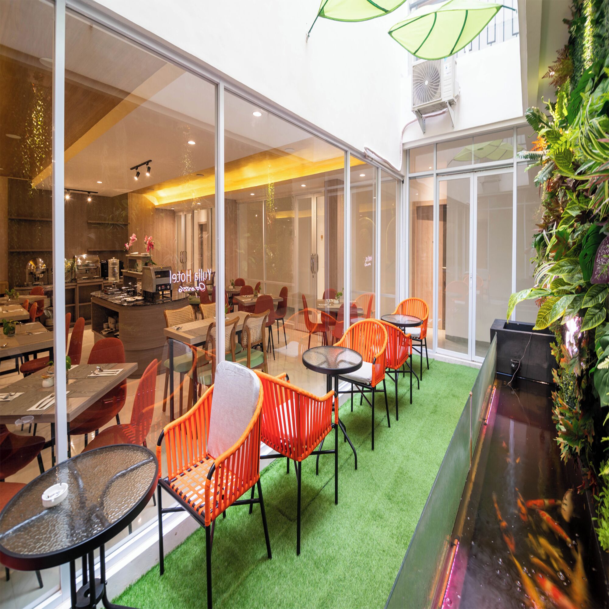 A modern restaurant with glass walls, indoor greenery, and orange chairs.