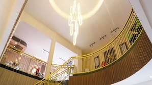 Ein modernes Interieur mit einer runden Leuchte an der Decke, einer geschwungenen Treppe mit gelben Geländern und einer Wand aus Holzpaneelen.