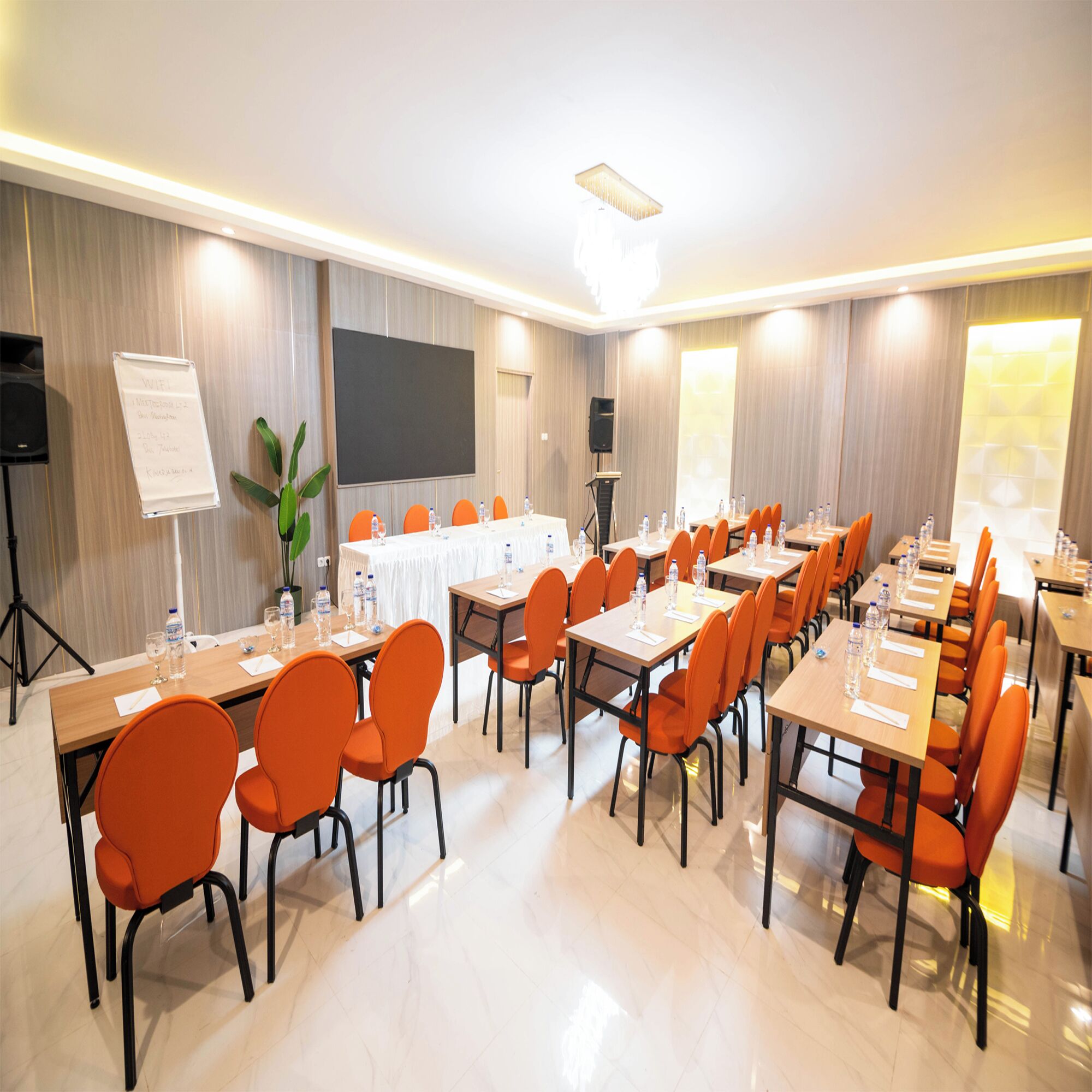 A conference room with multiple tables and orange chairs, equipped with water bottles and papers.