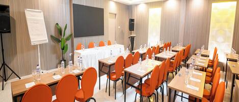 A conference room with multiple tables and orange chairs, equipped with water bottles and papers.