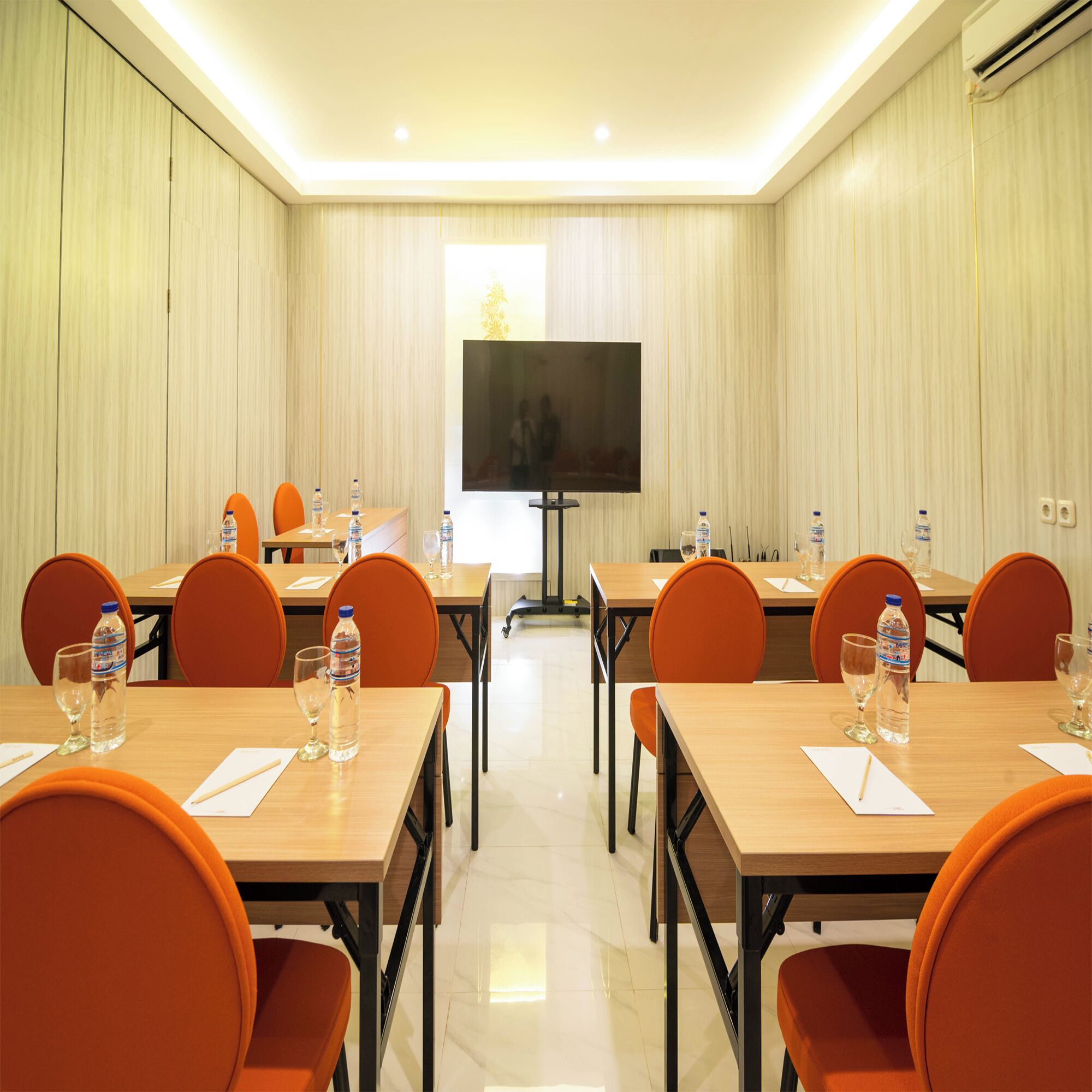 A conference room with a large flat-screen TV at the front, multiple tables with chairs, and water bottles on each table.