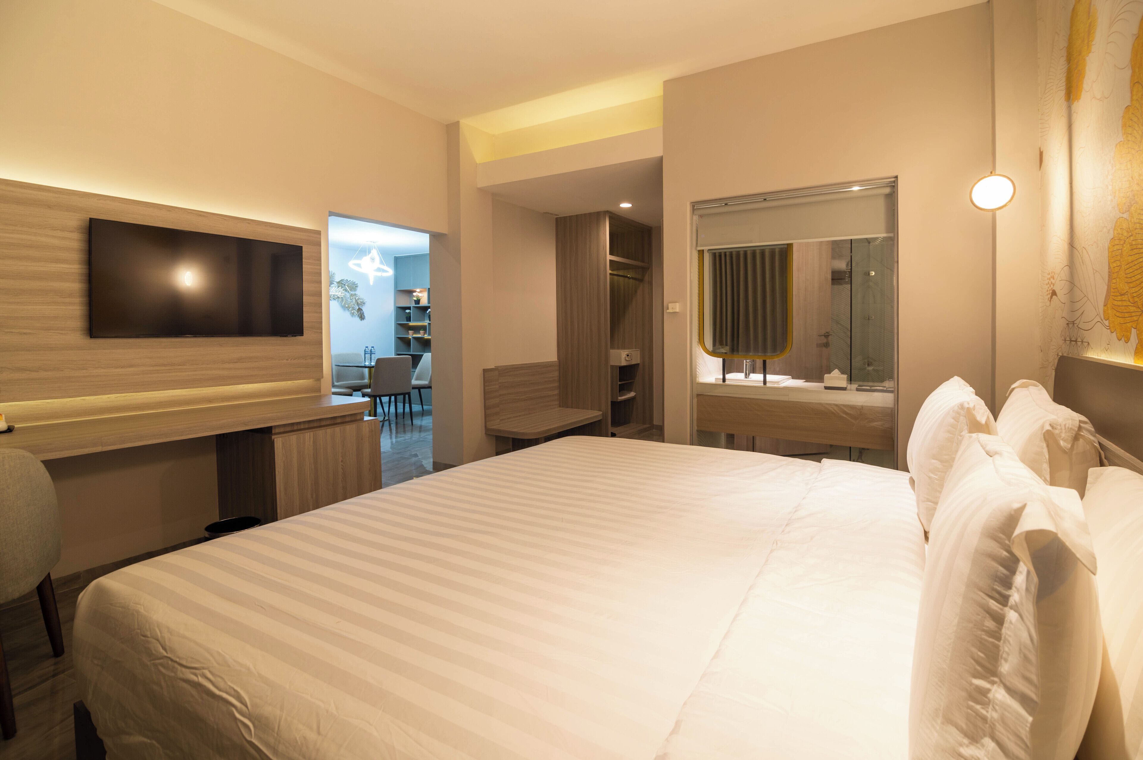 Ein Hotelzimmer mit einem großen Bett, einem Schreibtisch, einem Sessel, einem an der Wand befestigten Fernseher und einem Spiegel.