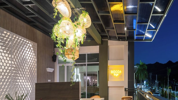 Ein Sitzbereich im Freien mit Tischen und Stühlen, einer modernen Leuchte und einem Neon-Schild für ein Café.