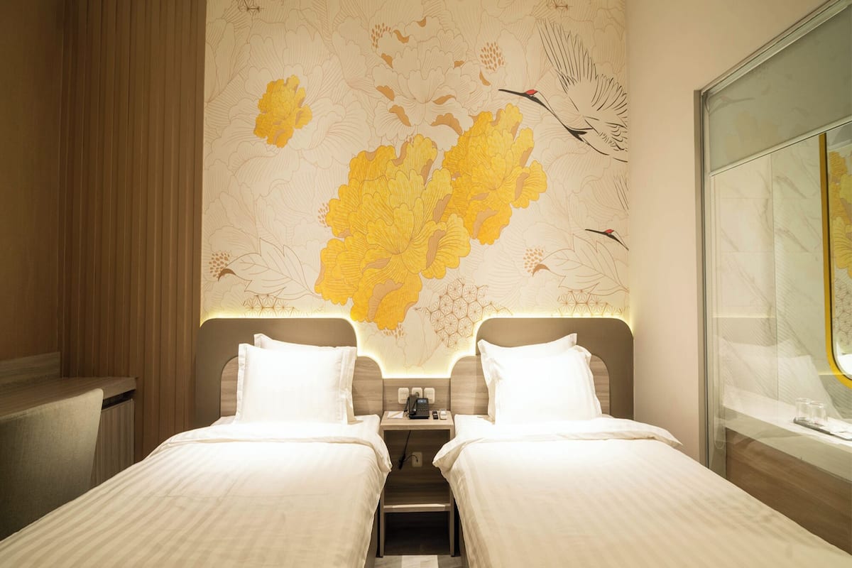 Een hotelkamer met twee bedden, een nachtkastje, een bureau en een groot raam.