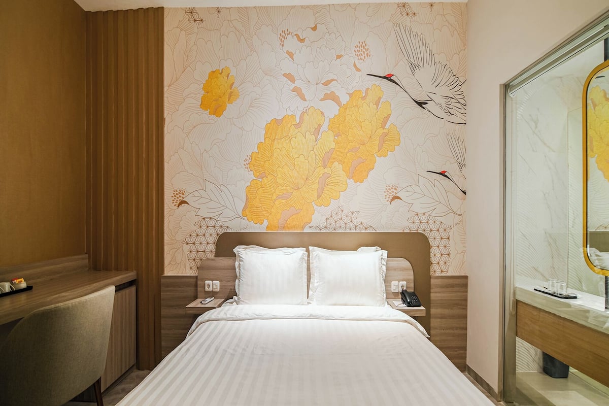 Een hotelkamer met een groot bed, een bureau en een muur met een bloemen- en vogelmural.