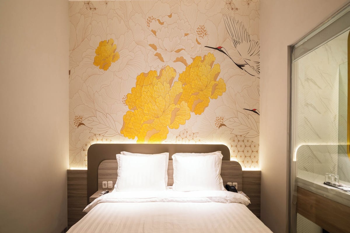 Een hotelkamer met een groot bed, een hoofdbord met een geometrisch patroon en een wanddecoratie met bloemen en vogelmotieven.